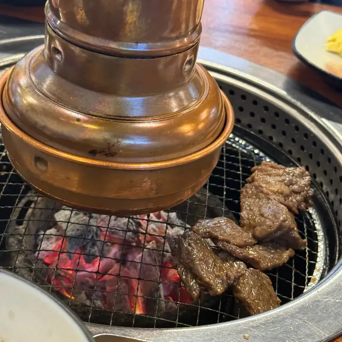 숯불 위에서 익고 있는 갈비살. 불꽃이 살짝 피어오르고 있다.