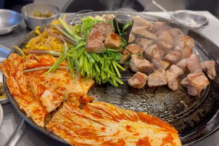 노릇하게 구워진 삼겹살과 목살 조각들, 그리고 솥뚜껑에 함께 구워진 김치