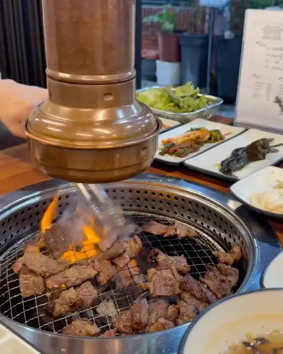 가게 안에서 숯불에 고기를 굽는 모습. 다양한 밑반찬이 테이블에 놓여있다.
