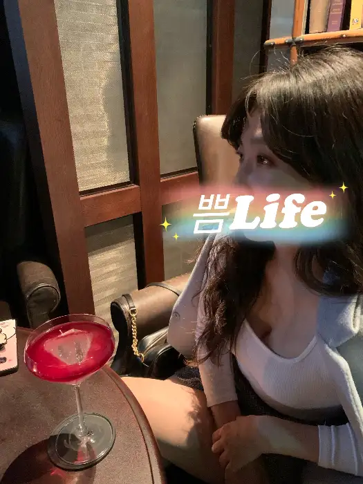 어두운 조명 아래 붉은색 칵테일과 함께 앉아있는 여성