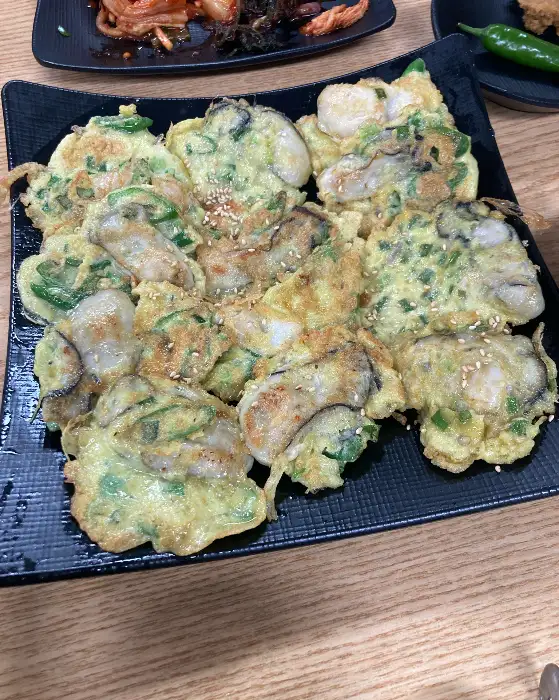 굴전 사진: 동그랗게 부쳐진 굴전 위에 쪽파와 깨가 뿌려져 있다. 굴 알갱이가 큼직하게 보인다.