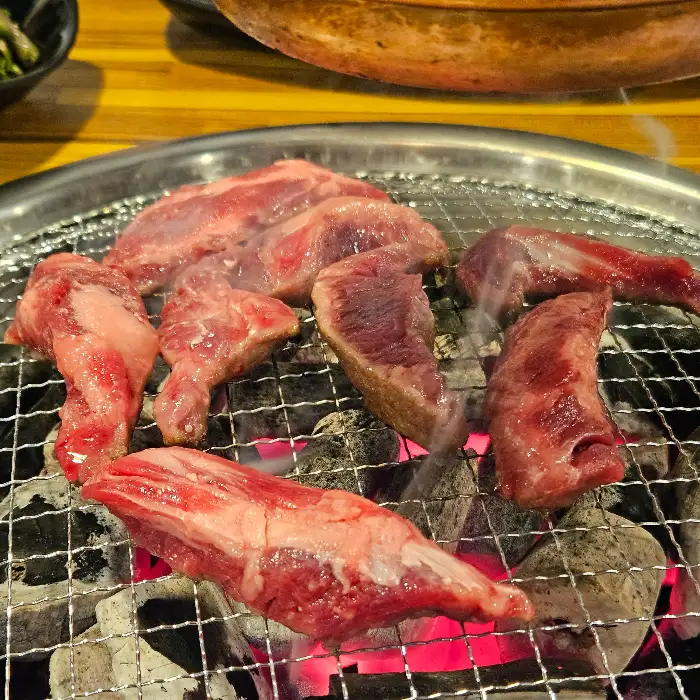 참나무 숯불 위에서 지글지글 구워지고 있는 갈비 조각들. 붉은 숯불의 열기가 느껴집니다.
