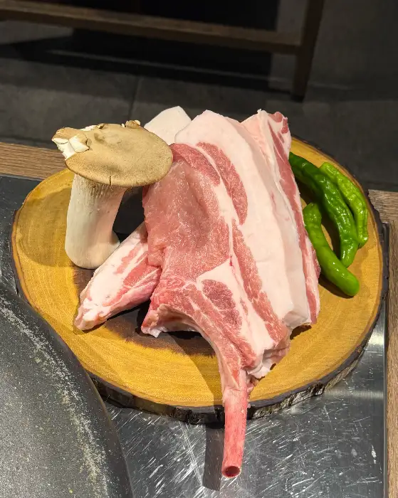 두툼한 흑돼지 목살, 오겹살, 그리고 팽이버섯과 고추가 놓인 모습.
