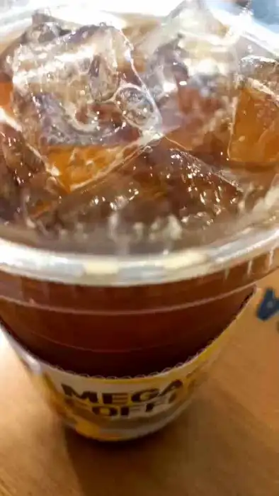 투명한 컵에 얼음과 커피가 담겨 있고, 컵 홀더가 씌워져 있는 모습. 컵 홀더에는 'MEGA COFFEE' 문구가 보인다.