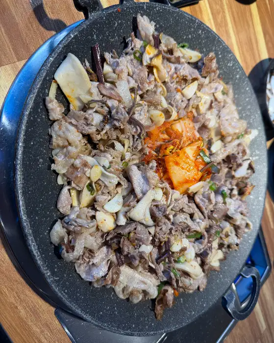 쟁반에 담긴 대패삼겹살과 함께 김치, 대파, 마늘 등이 볶아지고 있는 모습