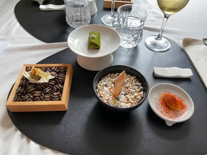 A collection of small dishes with various food items, including a square dish with dark chocolate-like material and a small pastry.