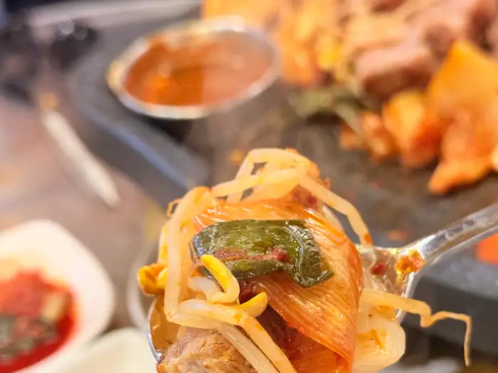 김치와 콩나물을 얹어 삼겹살을 집은 모습