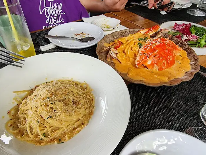 Two plates of pasta dishes on a table, one with a creamy sauce and crab meat, the other with a light sauce and breadcrumbs.