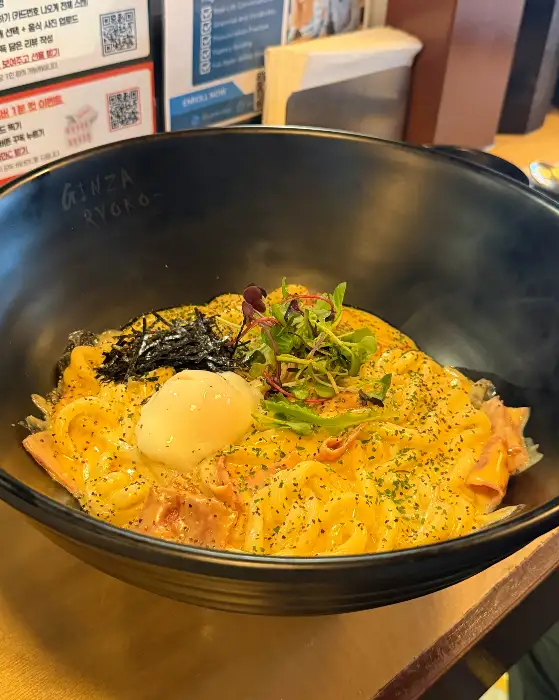 노란 소스가 덮인 면 요리 위에 수란과 김가루, 잎채소가 올라간 모습