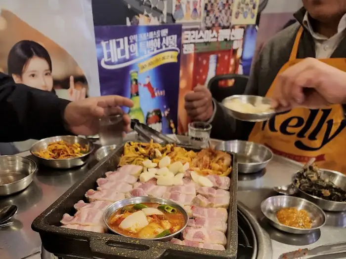 통삼겹살이 푸짐하게 담겨 나온 불판 위로 손이 뻗어 있습니다.