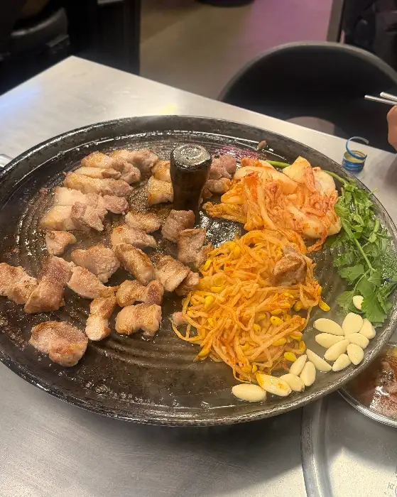 솥뚜껑 위에서 맛있게 익어가고 있는 삼겹살과 곁들임 음식들