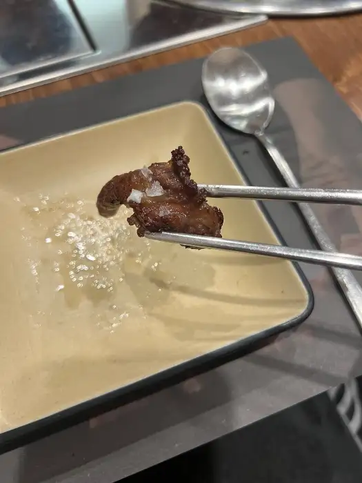 집게로 소금에 찍어 먹기 위해 집어 올린 고기 조각
