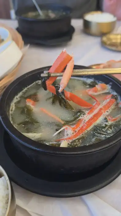 김이 모락모락 나는 홍게 미역국에 젓가락으로 홍게살을 건져 올리는 모습.