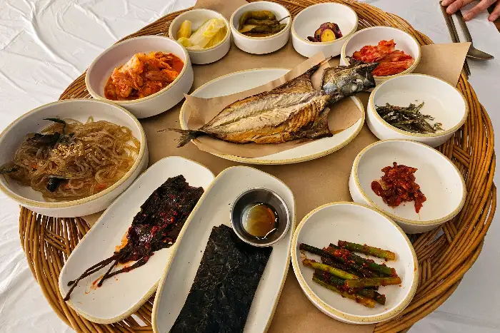 잘 구워진 생선구이가 담긴 접시와 함께 주변으로 다양한 밑반찬들이 차려져 있습니다.
