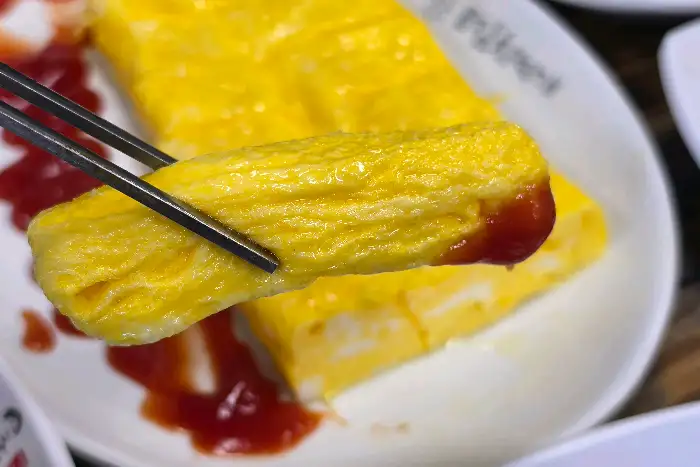 집게로 집어 올린 계란말이 조각
