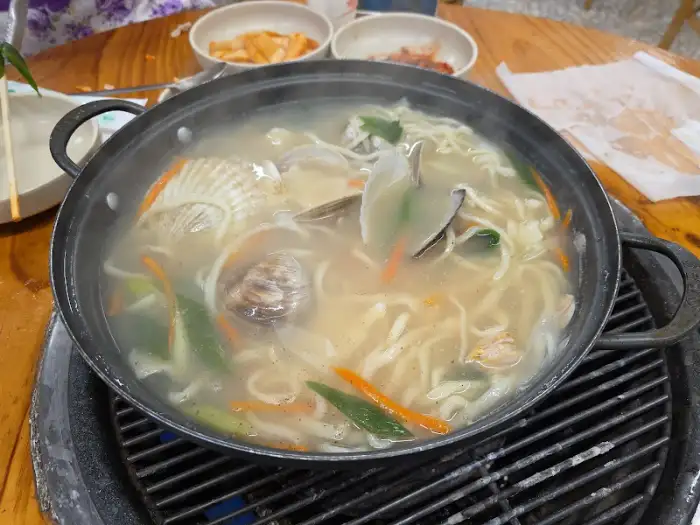 불판 위에서 맛있게 익어가는 조개구이. 김이 모락모락 피어오르고 있다.