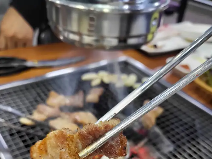 집게로 집어 올린 삼겹살 조각