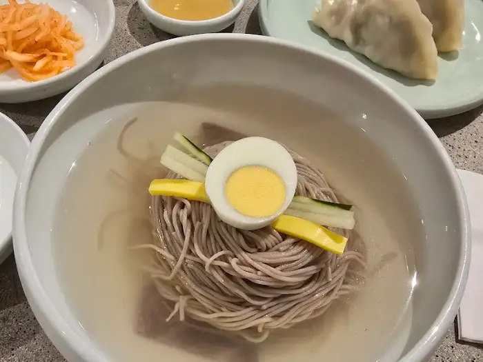 평양냉면 그릇의 클로즈업. 얇게 썬 메밀면과 맑은 육수가 보입니다.