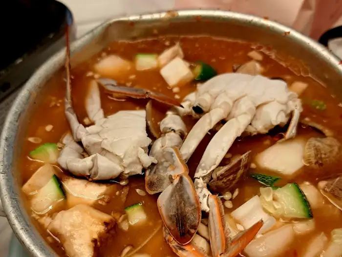 깊은 국물의 찌개 안에 게와 조개 등 해산물이 들어 있는 모습