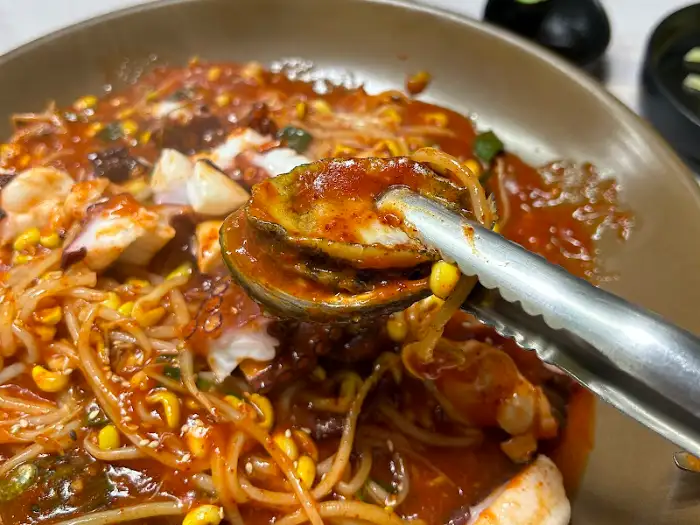 집게로 아구찜 속 문어 다리 하나를 집어 올리는 모습