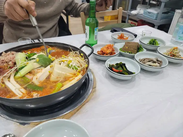 식탁 위 동태탕 냄비와 여러 반찬들이 놓여 있습니다. 한 사람이 숟가락으로 국물을 뜨고 있습니다.