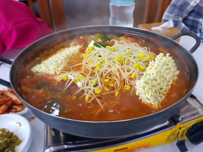 동태탕 냄비에 라면 사리가 두 덩이 들어가 있습니다. 콩나물이 그 위를 덮고 있습니다.