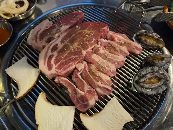 불판 위에서 삼겹살, 전복, 새송이버섯이 함께 구워지고 있다
