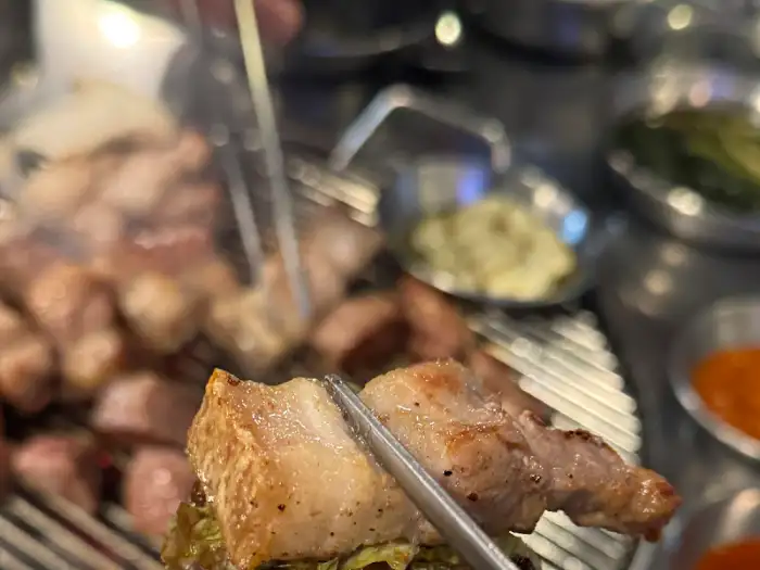 집게로 삼겹살 조각을 집어 상추 위에 올리는 모습