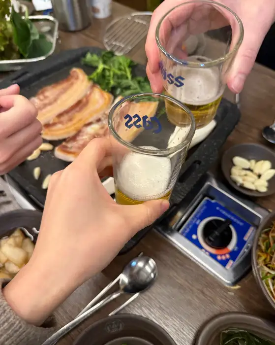시원한 맥주잔을 들고 건배하는 모습. 고기를 즐기며 행복한 시간을 보내고 있음을 보여줍니다.