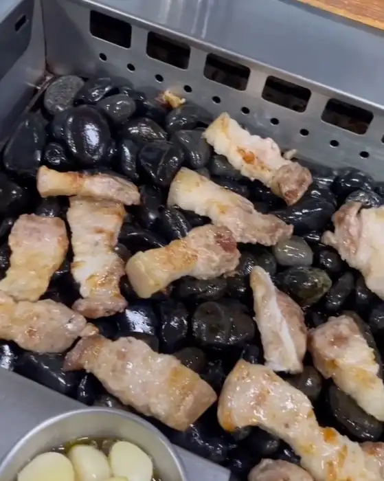 잘 익은 흑돼지 조각을 집게로 집어 올리는 모습