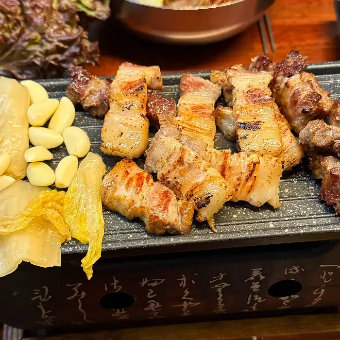 잘 구워진 삼겹살과 쌈채소, 마늘, 김치가 함께 놓여 있는 모습