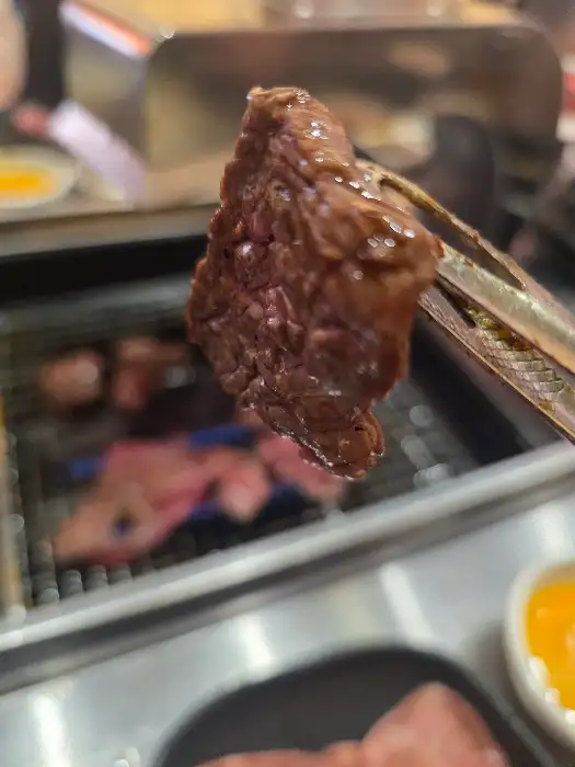 집게로 집어 올린 잘 구워진 고기 한 점