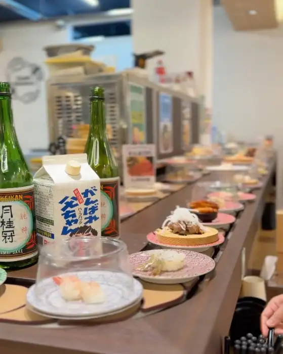회전 초밥 레일을 따라 이동하는 여러 초밥 접시들, 병맥주와 우유팩이 보임