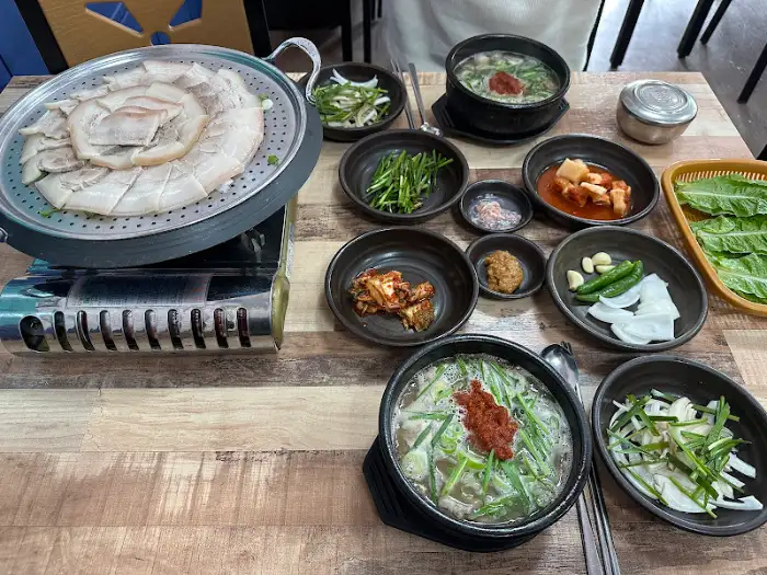 테이블 위로 국밥, 수육, 쌈 채소, 김치 등 푸짐하게 차려진 한 상차림이 보입니다. 다양한 메뉴들이 시각적인 만족감을 선사합니다.