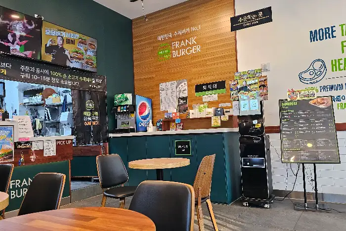 프랭크버거 매장 내부, 주문 카운터와 메뉴판, 테이블이 보인다.