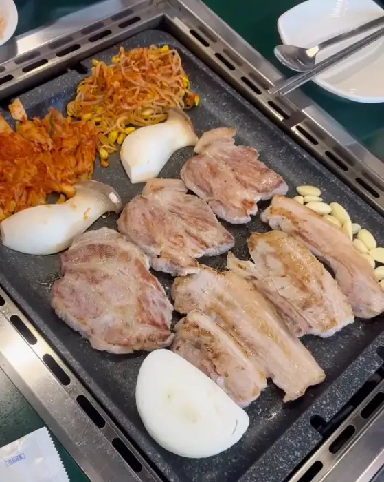 돌판 위에 올려진 삼겹살, 목살, 그리고 곁들임 채소