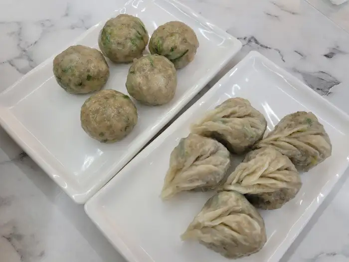 직사각형 접시에 굴림만두와 찐만두가 각각 담겨 있습니다. 굴림만두는 둥근 형태이고, 찐만두는 잎사귀 모양으로 빚어져 있습니다.