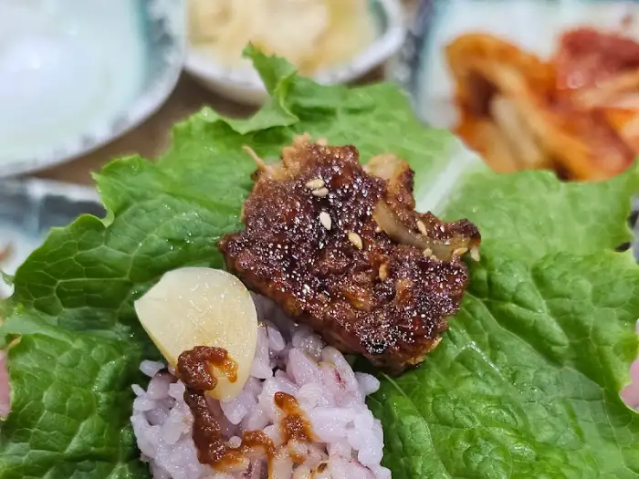 쌈 채소에 밥과 떡갈비, 마늘을 싸 먹는 모습