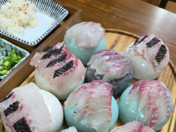여러 개의 둥근 밥 뭉치 위에 얇게 썬 생선회가 올려져 있는 모습