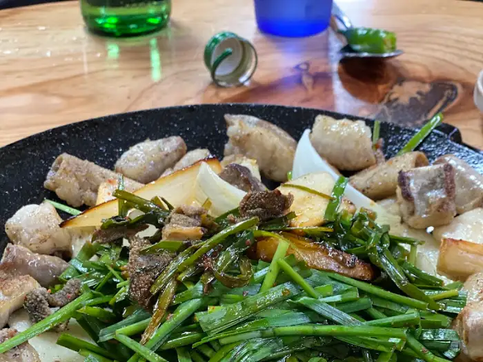 테이블 위에 놓인 곱창과 소주병, 파란 컵이 선명하게 보이는 클로즈업 사진.