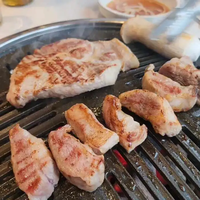 다양한 부위의 돼지고기가 그릴 위에서 맛있게 익어가고 있는 모습