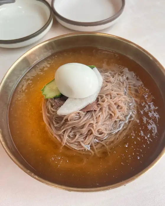 놋그릇에 담긴 평양냉면, 달걀 반쪽과 오이, 고기 고명이 올려져 있습니다.