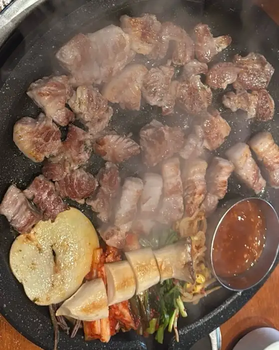 돌판 위에서 지글지글 익어가는 삼겹살과 목살, 그리고 곁들여진 버섯과 김치가 먹음직스럽습니다.