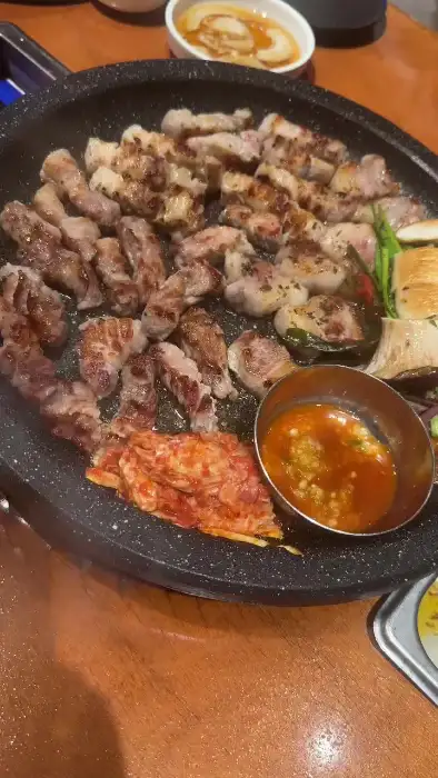 다양한 종류의 고기가 돌판 위에서 익고 있으며, 곁들여진 김치와 콩나물, 버섯 등이 보입니다.