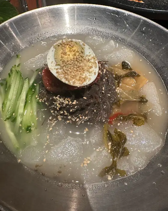 시원한 냉면이 그릇에 담겨 있습니다. 오이와 달걀, 고명이 고명으로 올려져 있습니다.