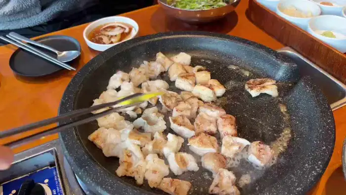 돌판 위에서 노릇하게 구워지고 있는 대창과 곁들임 채소들의 모습입니다.