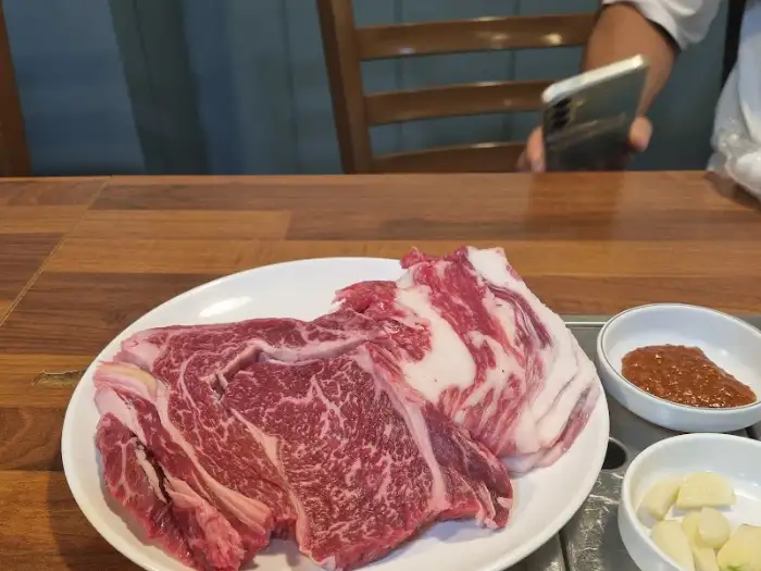 두툼한 소고기 구이가 접시에 담겨 있고, 곁들임 양념장이 함께 놓여 있다.