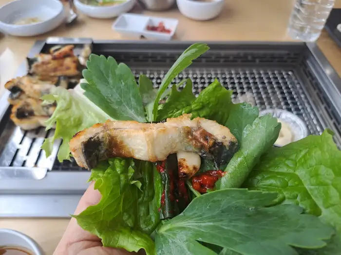 장어 한 점을 쌈 채소와 함께 손으로 감싸고 있는 모습