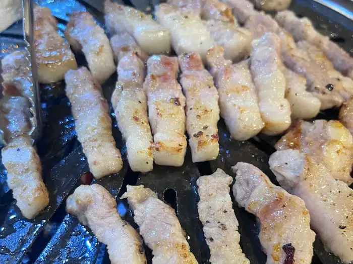 노릇하게 구워진 삼겹살이 불판 위에서 맛있게 익어가고 있는 모습