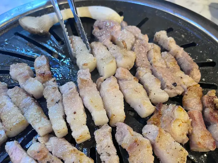 잘 구워진 꺼먹돼지 삼겹살과 목살이 불판 위에 가득 올려져 있다